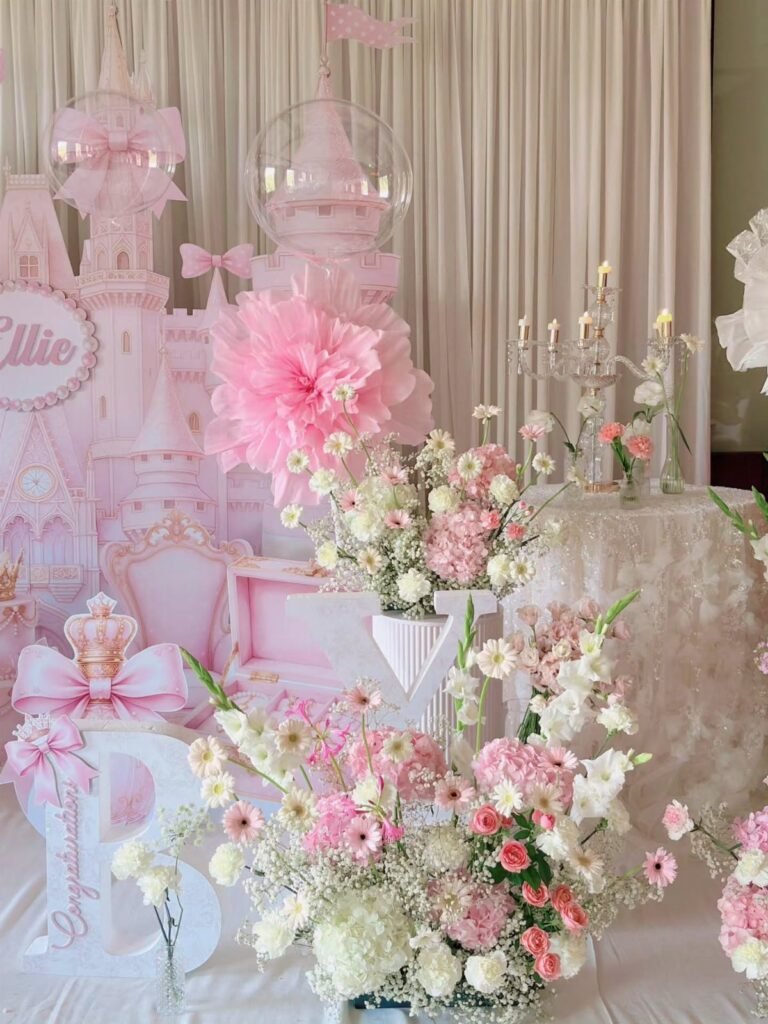 Pink birthday decorations featuring a castle backdrop, large paper flowers, and white and pink floral arrangements.