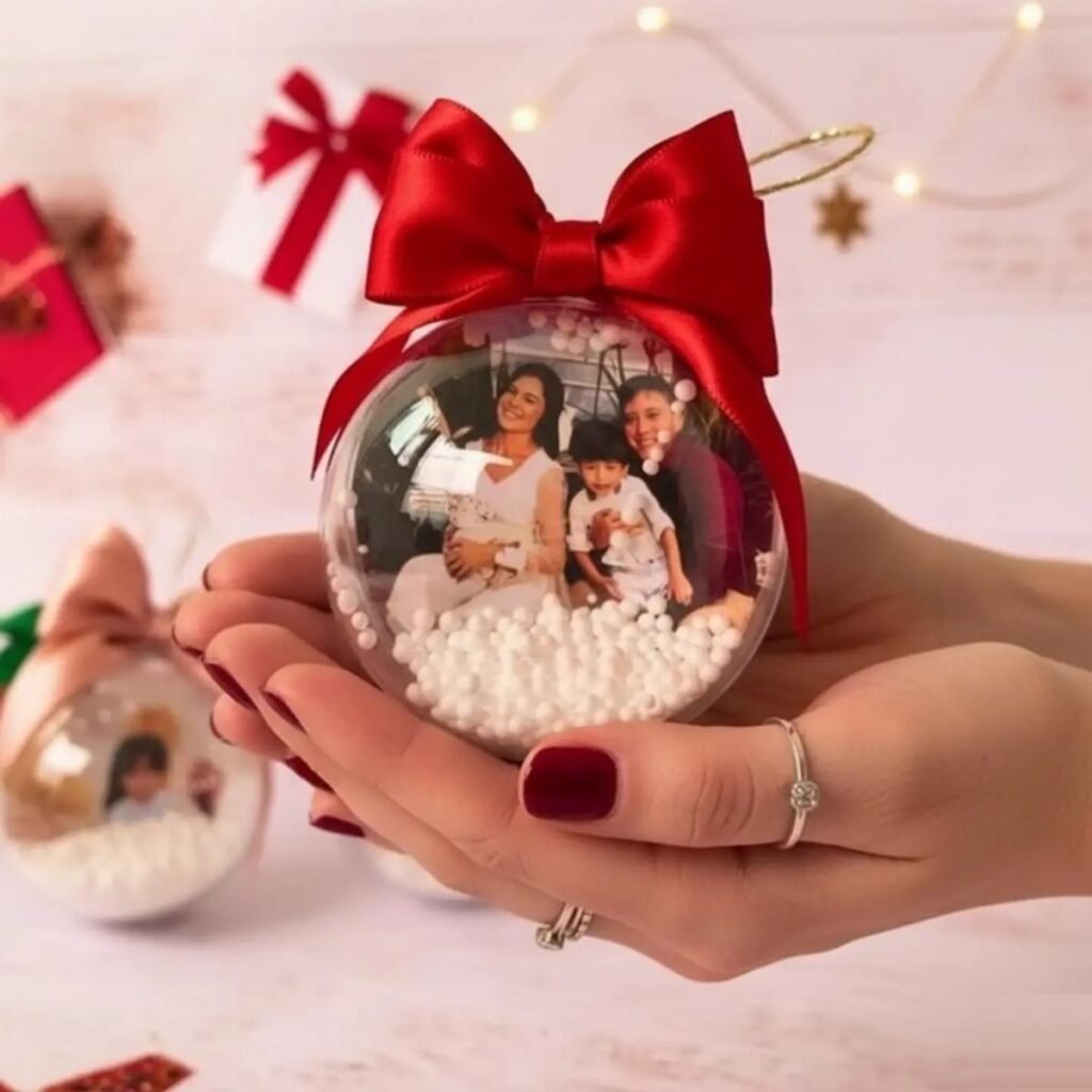 Hands holding a clear Christmas ornament featuring a family photo and white beads with a red bow.