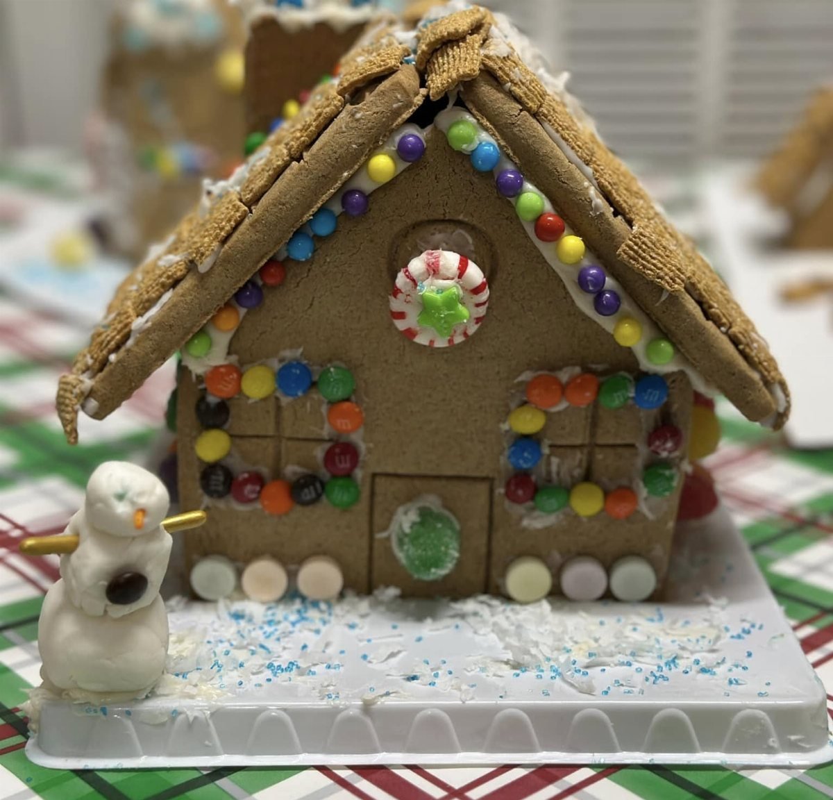 A decorated gingerbread house with colorful candies and a small icing snowman on a festive base.
