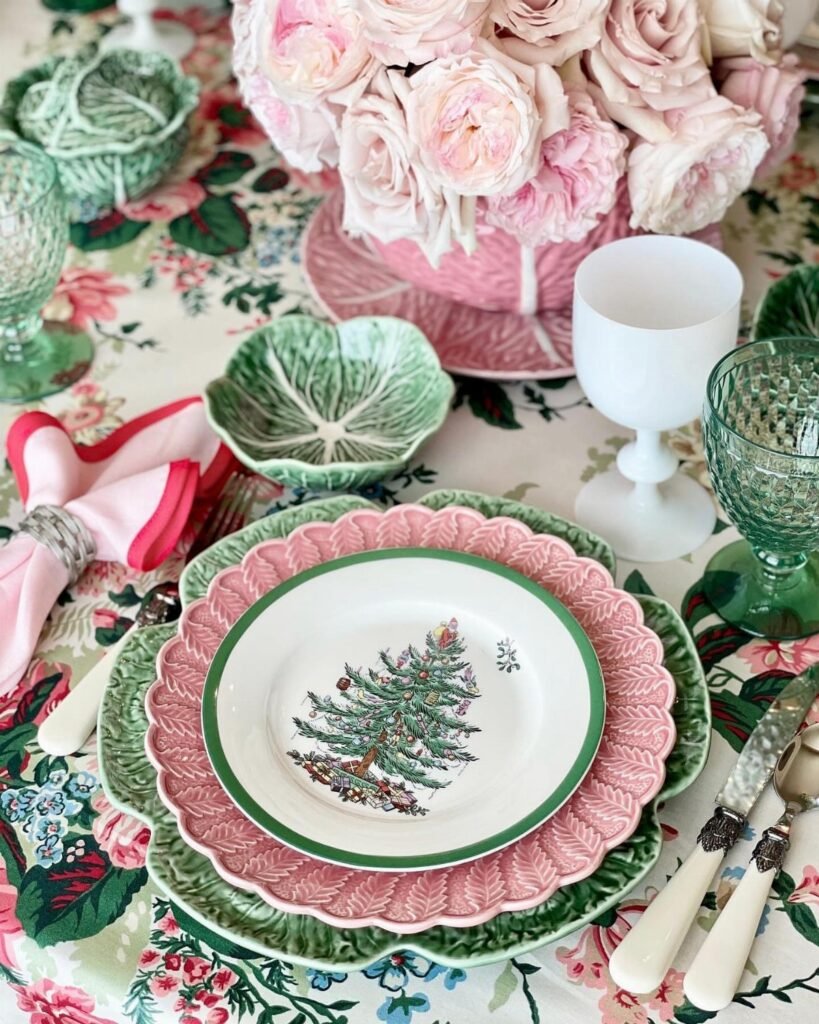 Layered scalloped plates in pink and green with a Christmas tree design on a floral tablecloth.