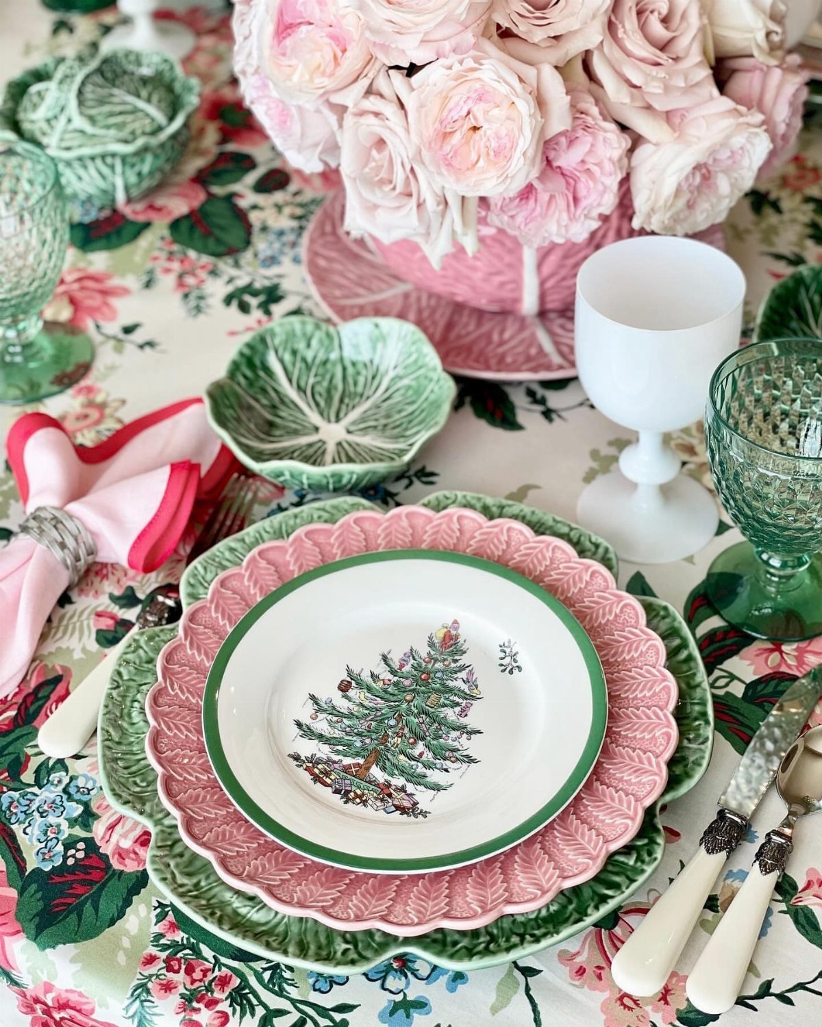 Layered scalloped plates in pink and green with a Christmas tree design on a floral tablecloth.