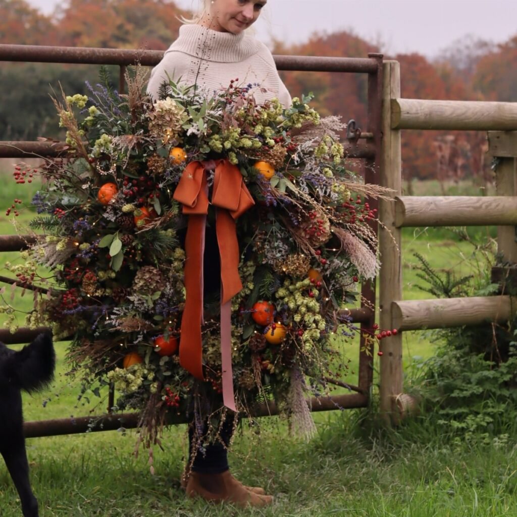 A large natural wreath with orange accents and a rust ribbon held by a person.