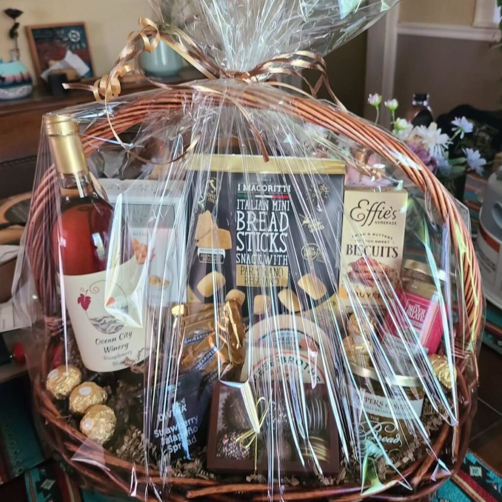 A wicker gift basket filled with wine, breadsticks, biscuits, and various gourmet food items.