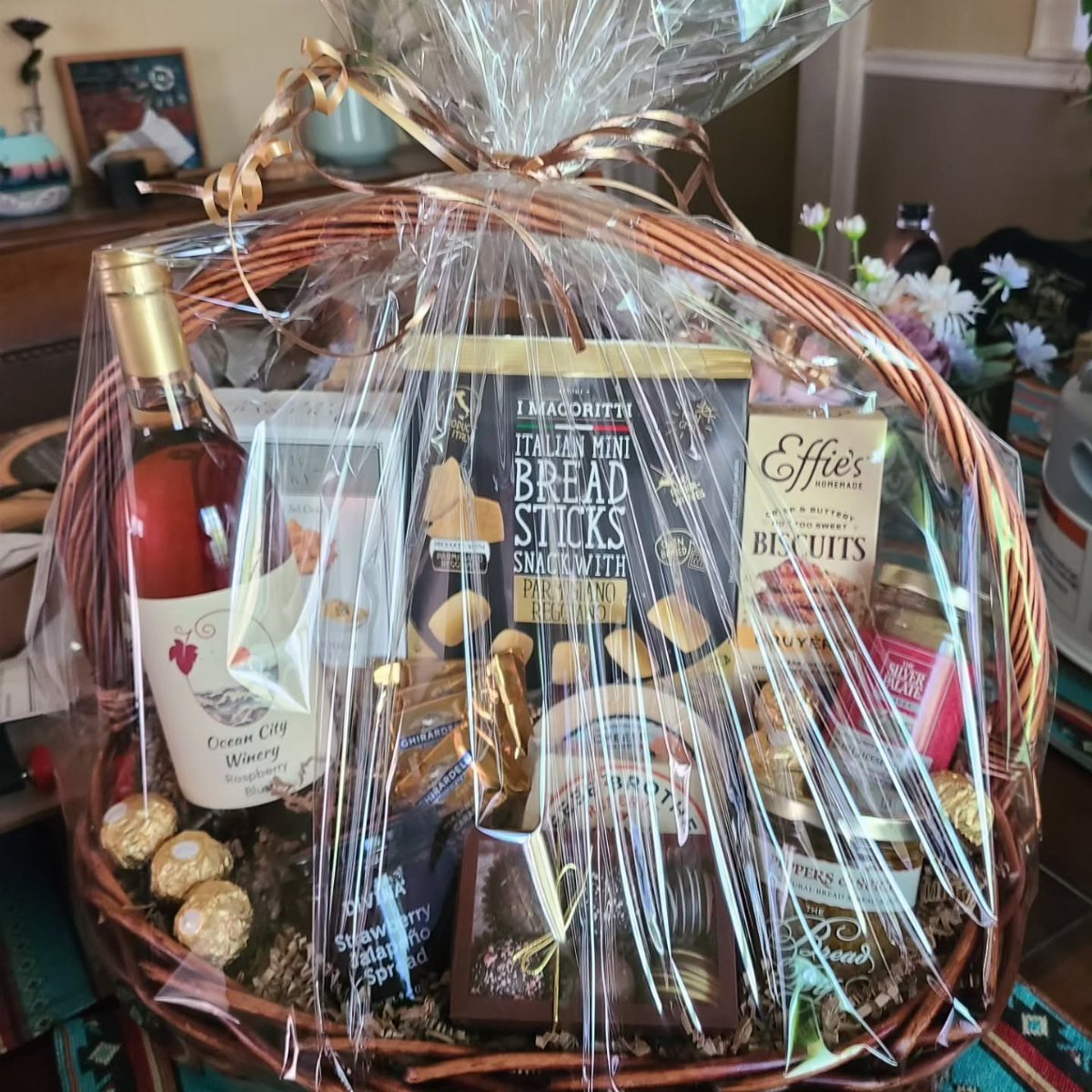 A wicker gift basket filled with wine, breadsticks, biscuits, and various gourmet food items.