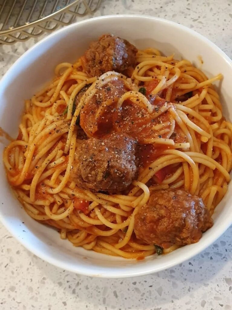 Spaghetti with tomato sauce and large meatballs served in a white bowl.