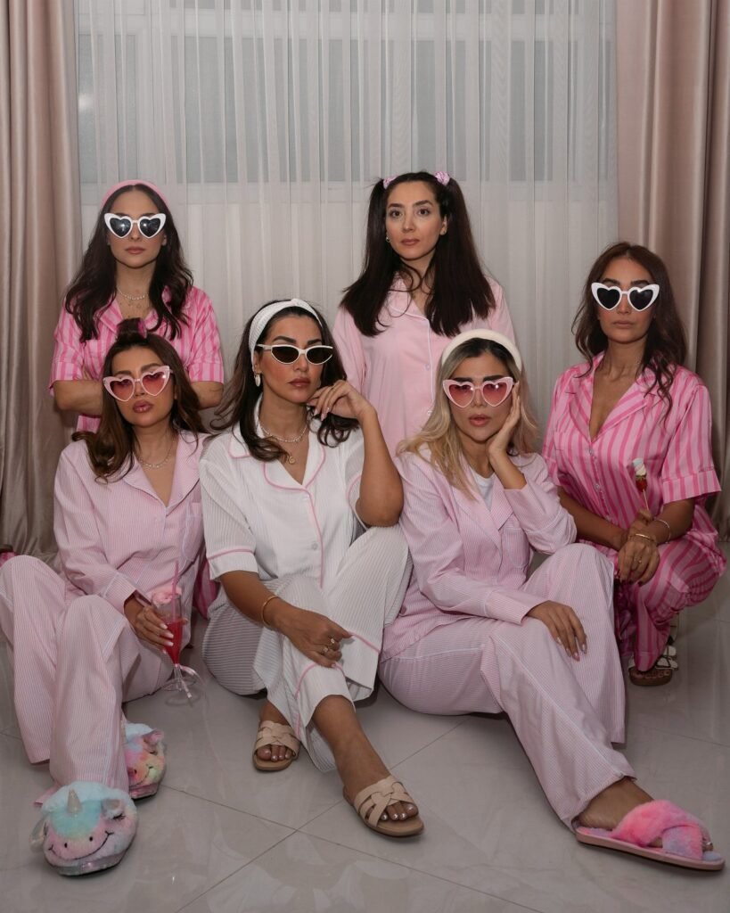 Six women wearing pink pajamas and heart-shaped sunglasses posing together for a group photo.