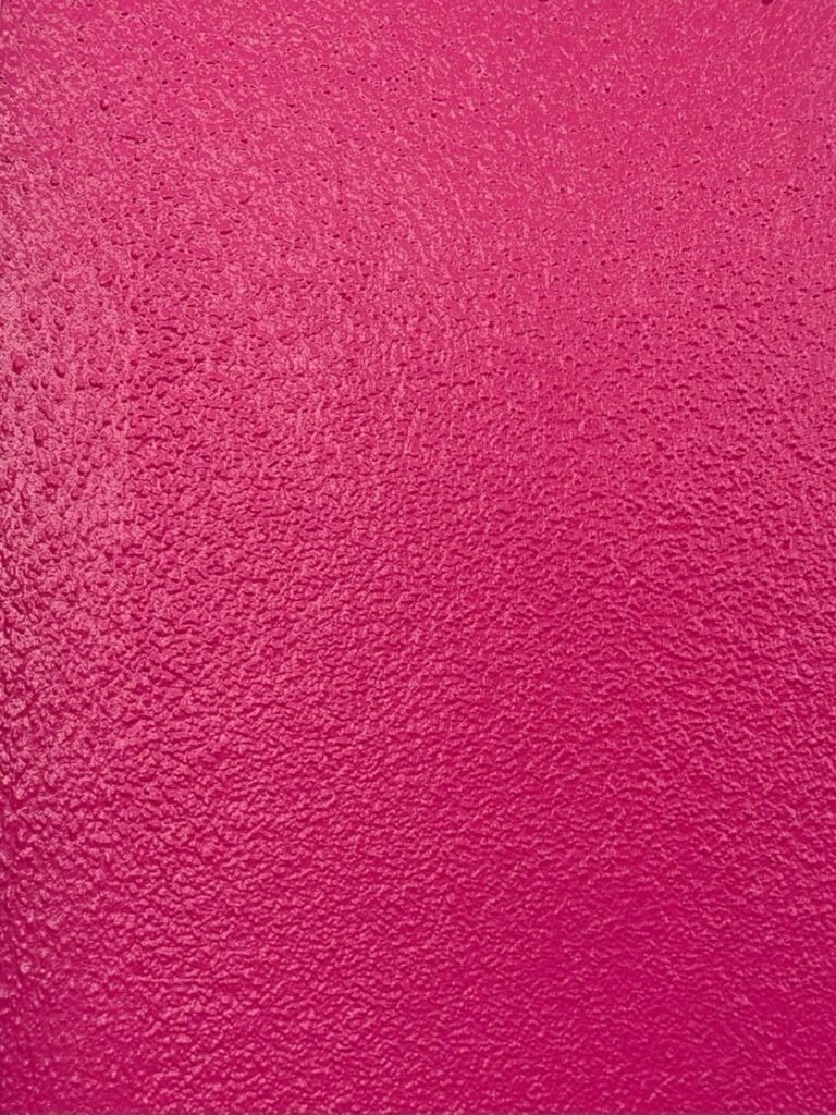 A textured, solid hot pink surface with a granular, unevenly painted finish.